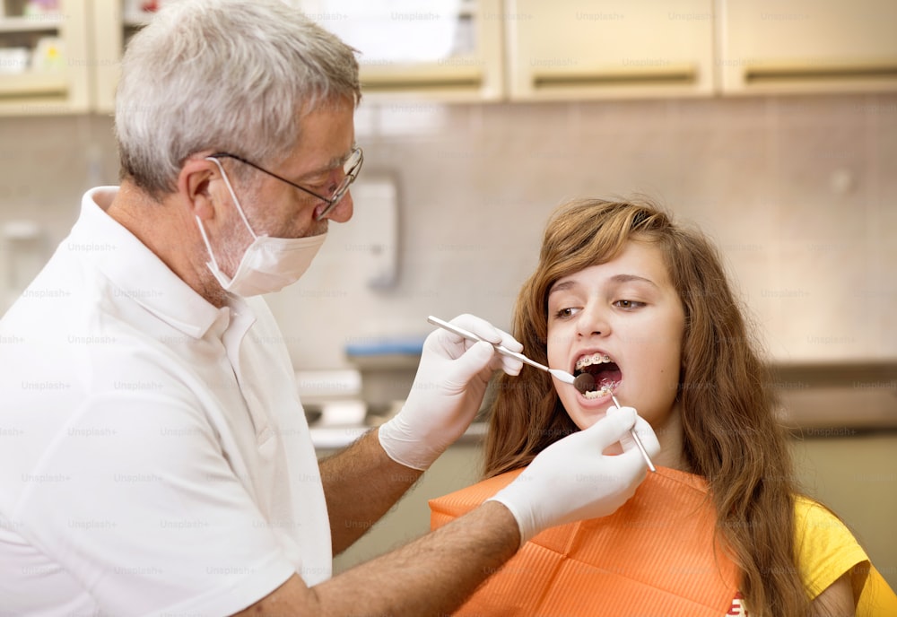 Teenage girl with the braces on her teeth is having a treatment at dentist