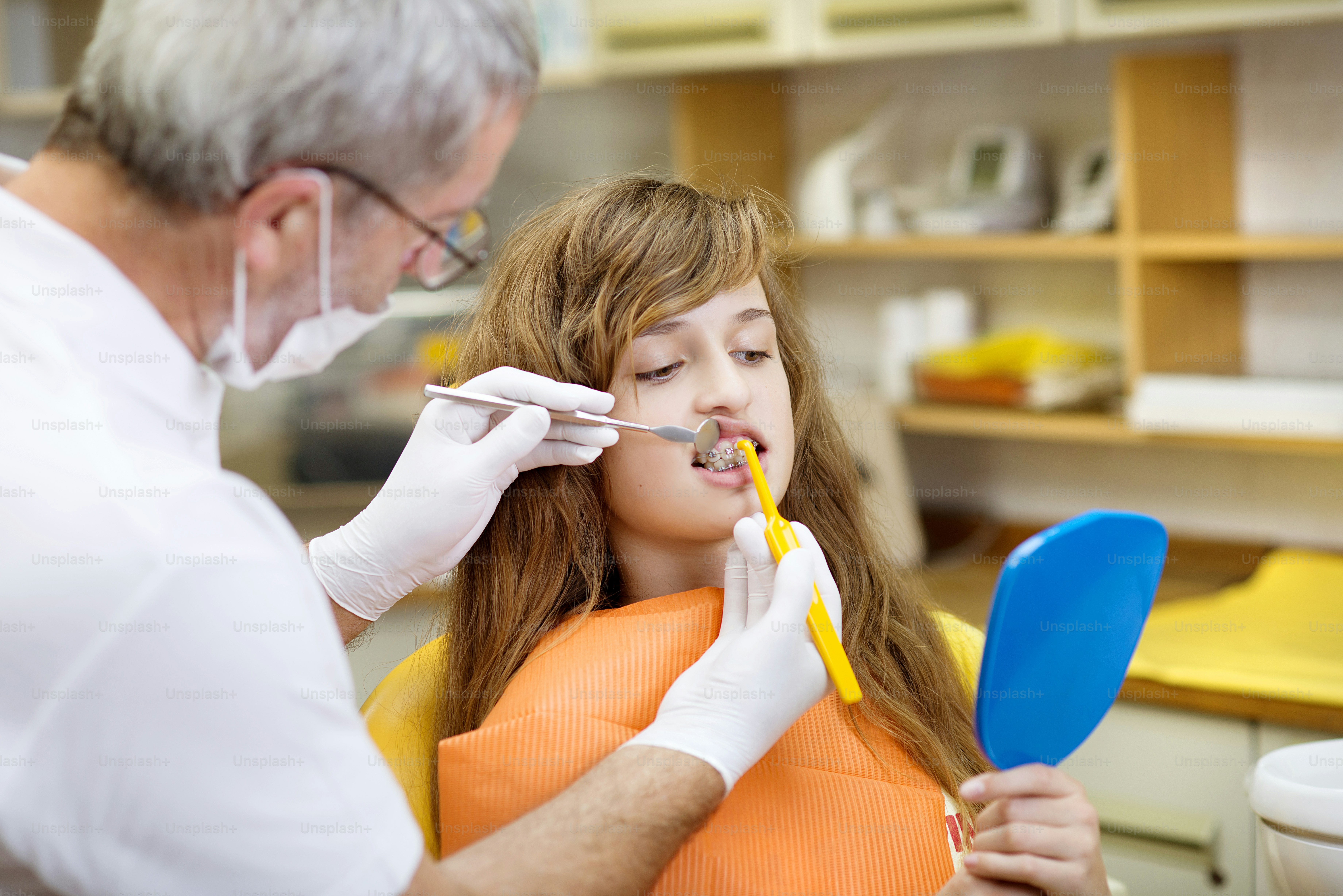 Teenage girl with the braces on her teeth is having a treatment at dentist