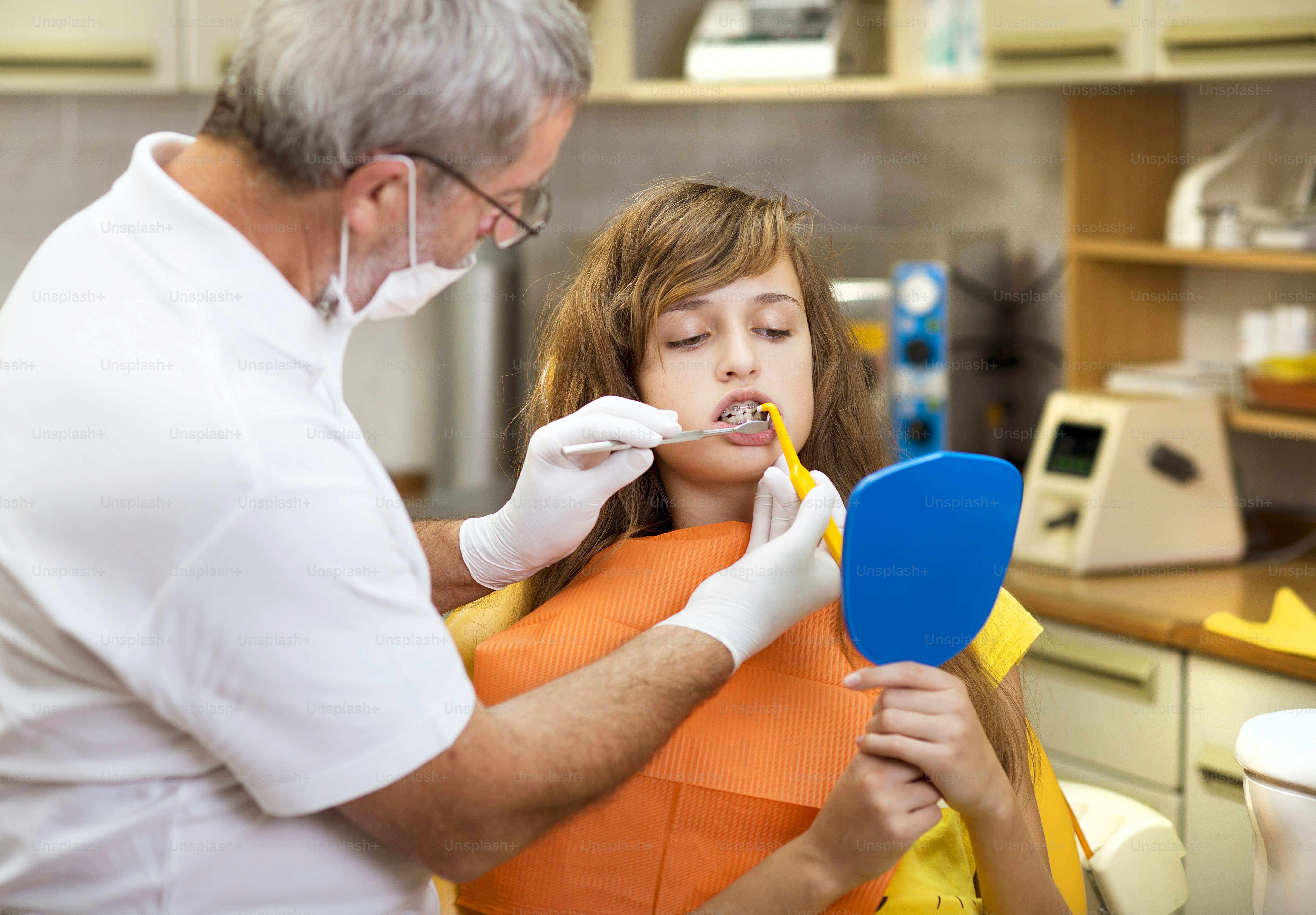 Teenage girl with the braces on her teeth is having a treatment at dentist