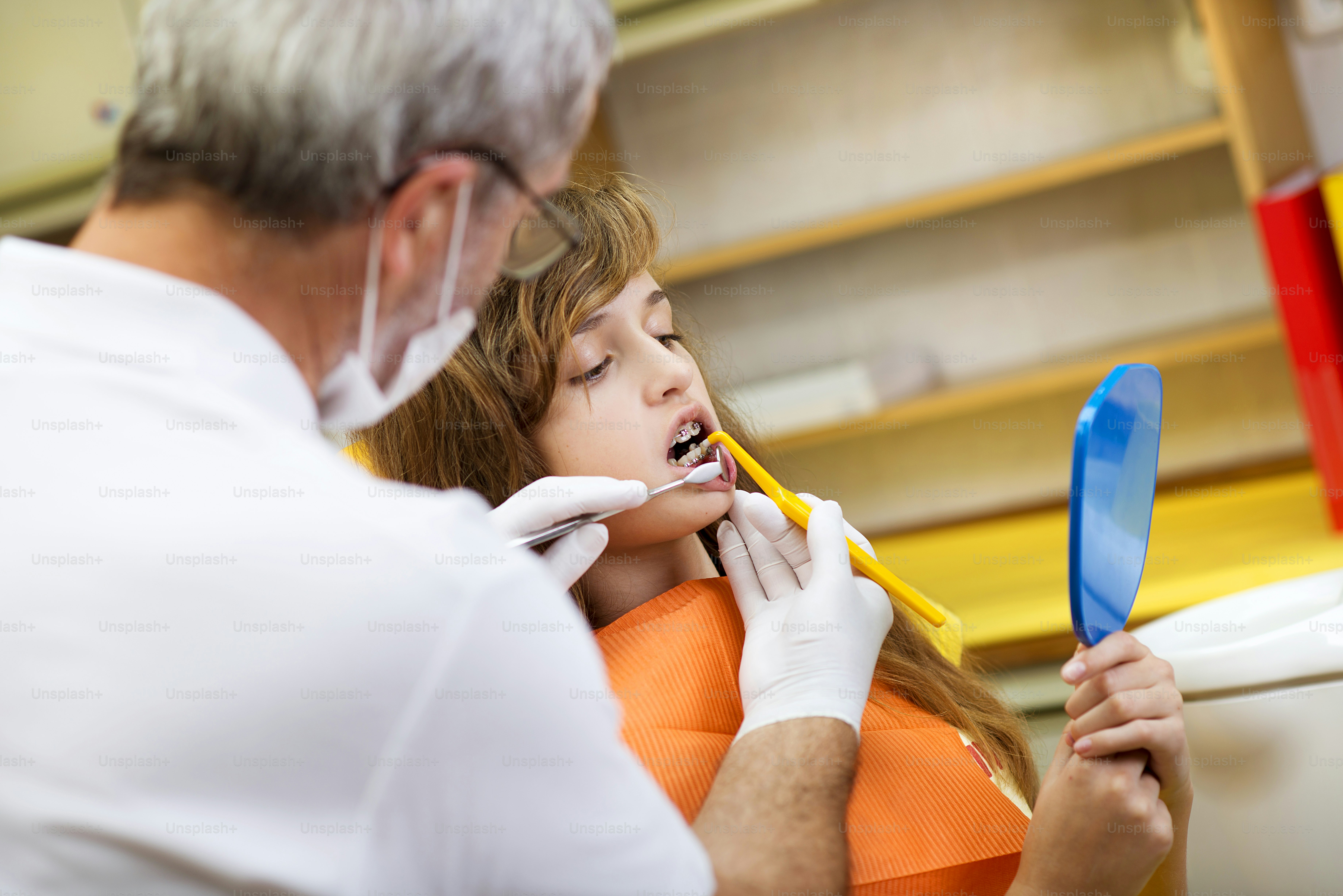 Teenage girl with the braces on her teeth is having a treatment at dentist