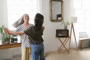 A happy senior grandmother with teenage granddaguhter dancing together at home.