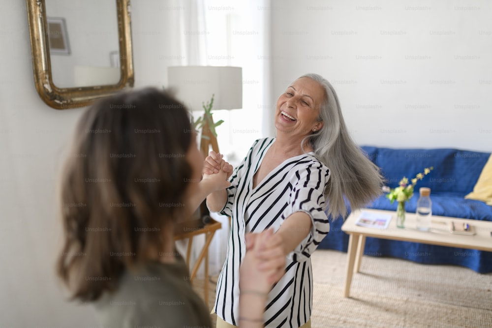 A happy senior grandmother with teenage granddaguhter dancing together at home.