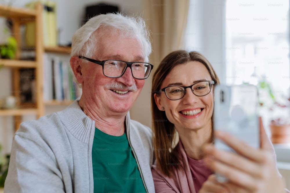 Eine erwachsene Tochter, die ihren älteren Vater zu Hause besucht und ein Selfie macht.