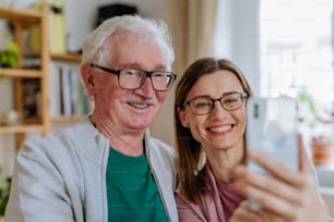 Una hija adulta visitando a su padre mayor en casa y tomándose una selfie.