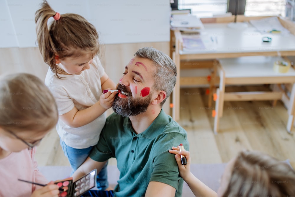 Three little girls putting on make up on their father, a fathers day with daughters at home.