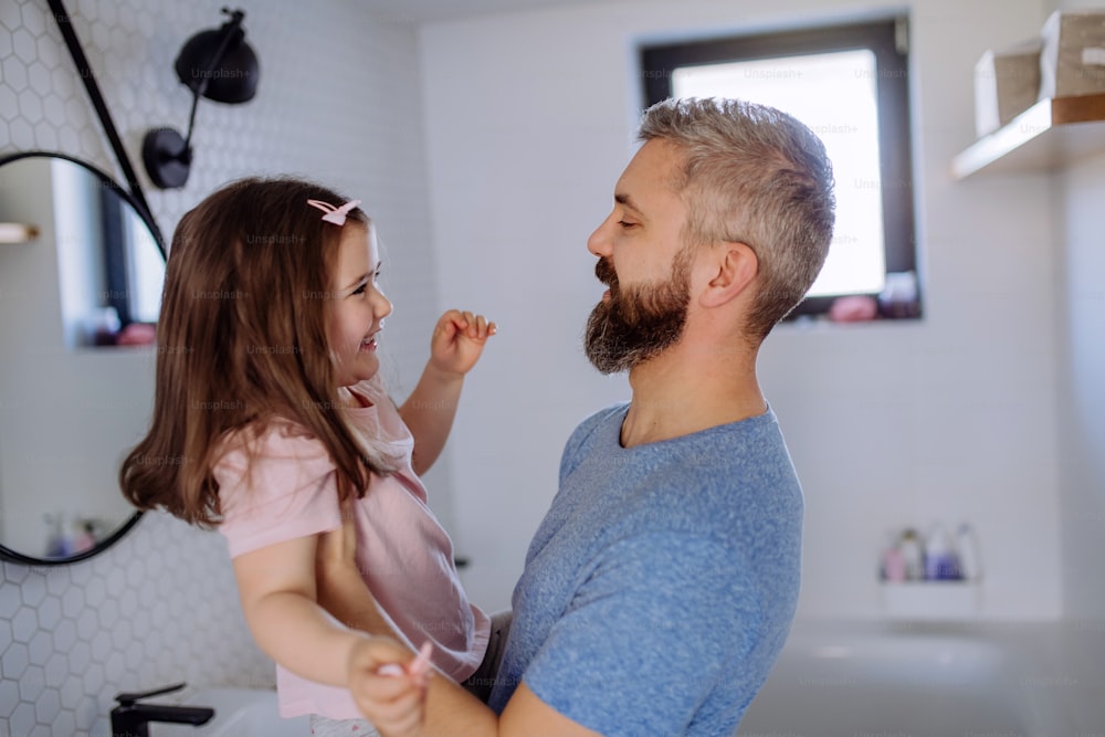 Un padre felice con la sua piccola figlia in bagno, concetto di routine mattutina.