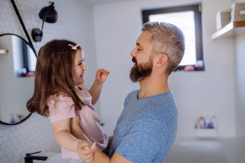 Un padre feliz con su hija pequeña en el baño, concepto de rutina matutina.