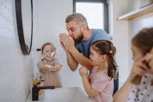 A father having fun blowing bubbles from soap in bathroom with his little daughters.