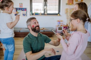 Three little girls putting on make up on their father, a fathers day with daughters at home.