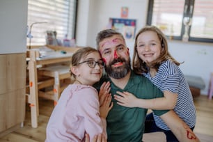 Two little girls putting on make up on their father, a fathers day with daughters at home.