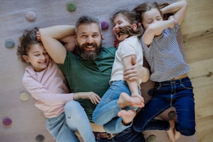 Una vista superior de un padre alegre con tres hijas pequeñas acostadas juntas en el suelo en casa.