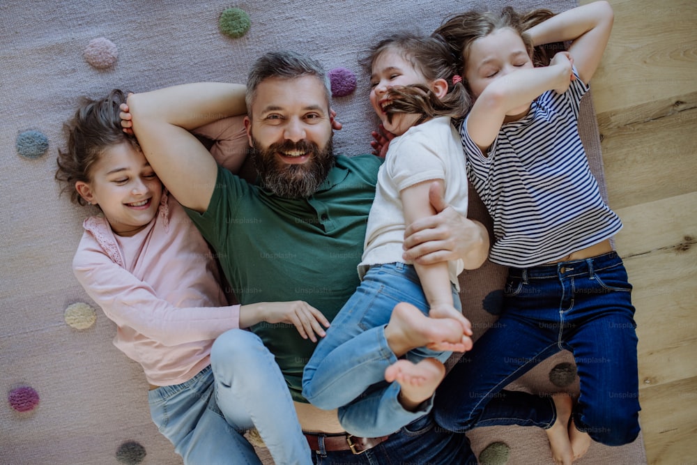A top view of cheerful father with three little daughters lying on floor together at home.