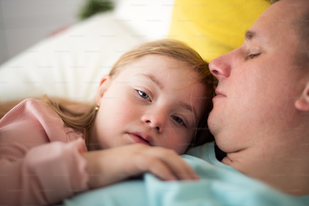 Um pai descansando com sua filhinha com síndrome de Down na cama em casa.
