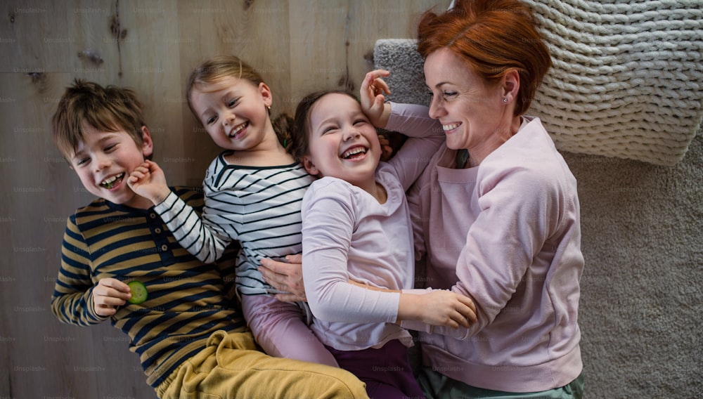 A top view of cheerful mother with three little children lying on floor together at home.