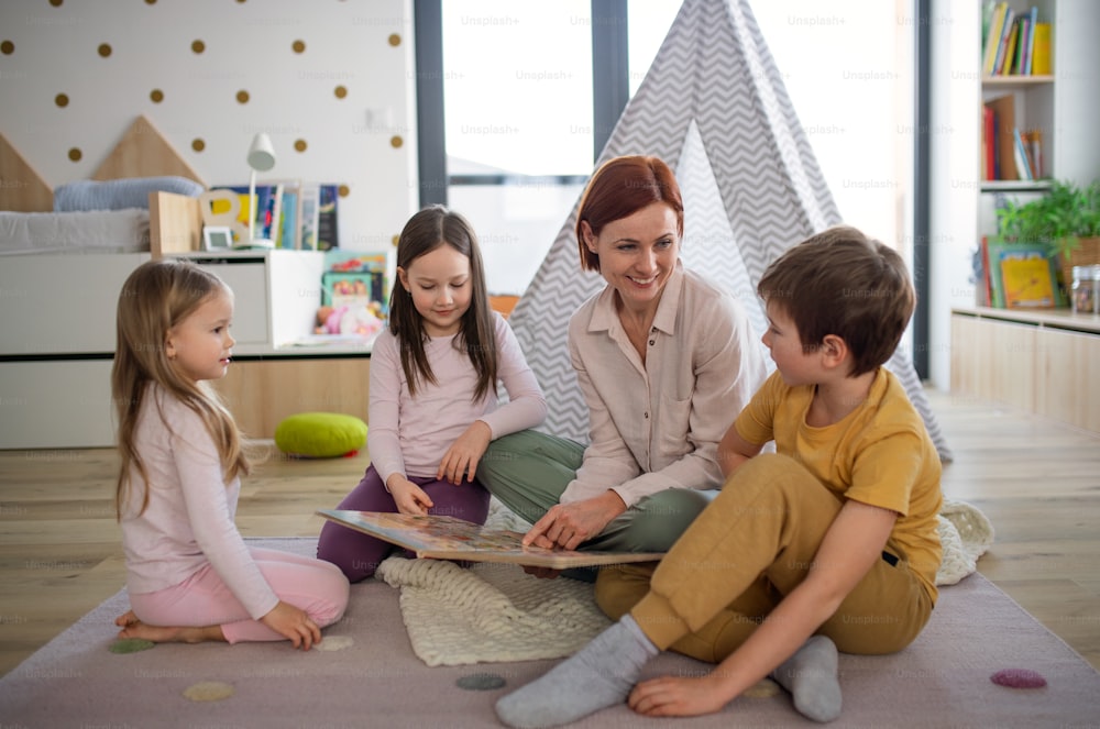 Une mère joyeuse de trois petits enfants qui leur lit un livre à la maison.