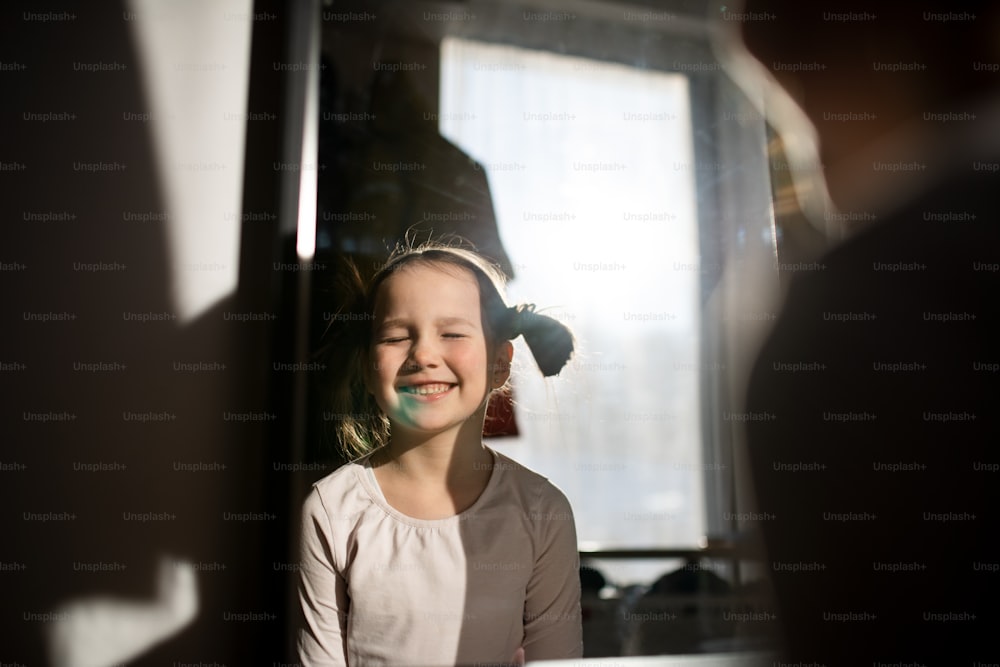 Uma garotinha com mancha azul no rosto sorrindo com os olhos fechados em casa.