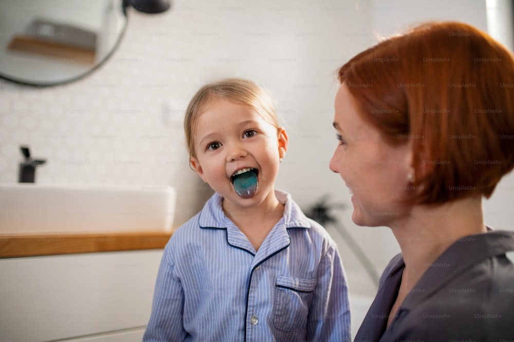 Una bambina attaccata mostrando la sua lingua blu alla madre nel bagno di casa.