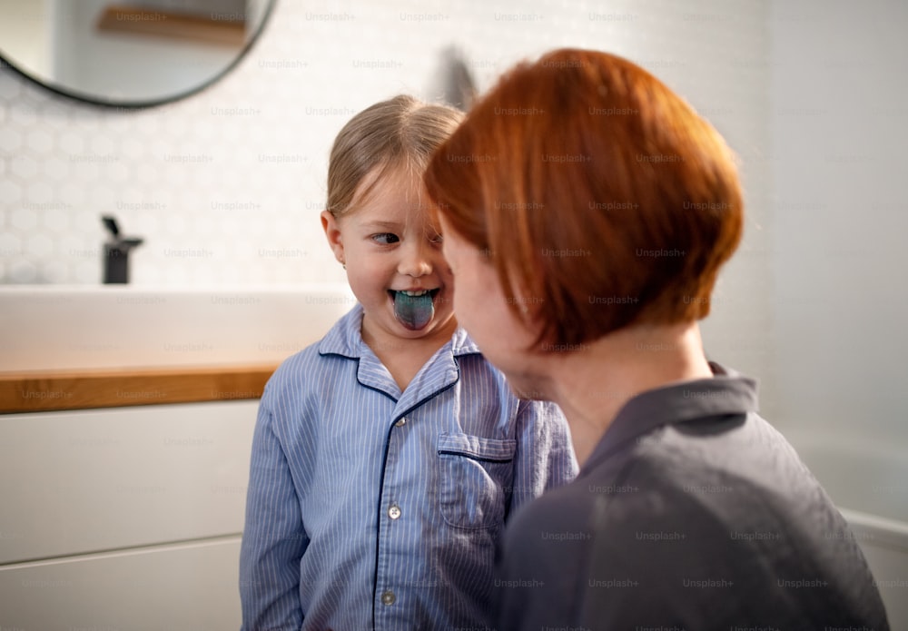 Uma garotinha furando mostrando sua língua azul para a mãe no banheiro de casa.
