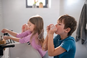 Llittle children in a bathroom, washing hands and doing bubbles from soap.