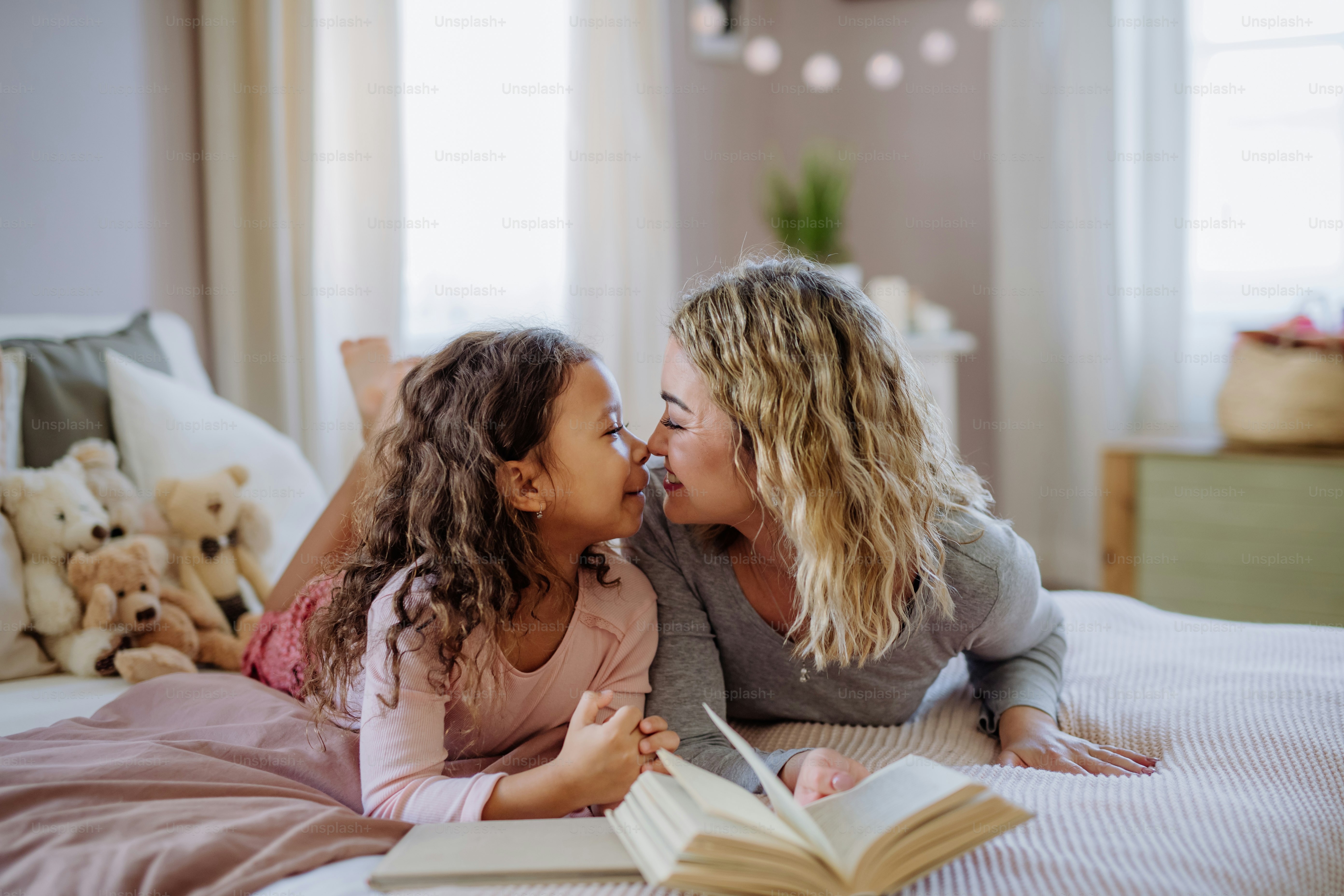 A happy mother with her little daughter lying on bed and tlooking at each other when reading