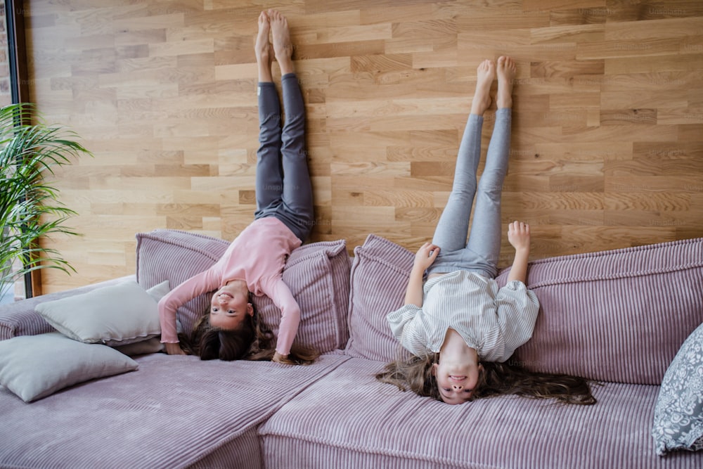 Happy little sisters doing head stand on a sofa at home.