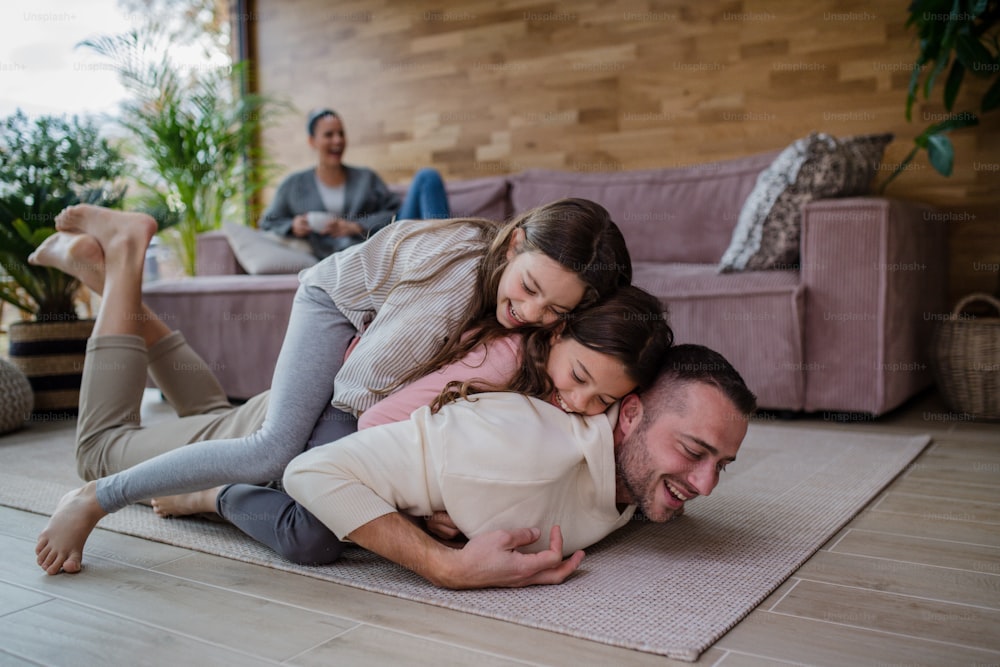 Two happy sisters having fun with a father, lying on his back with mother at background at home