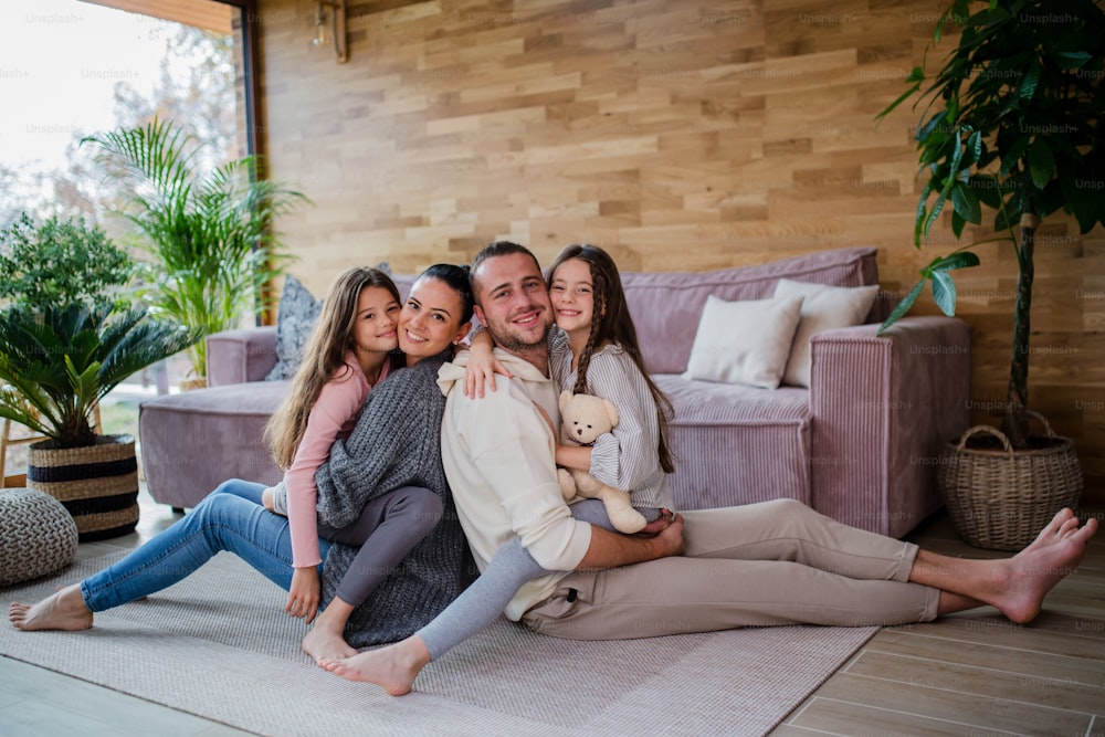 Two happy sisters with a mother and father sitting on floor hugging and looking at camera at home