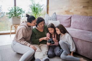 Two happy sisters with a mother and grandmother sitting on floor and learning to use camera at home