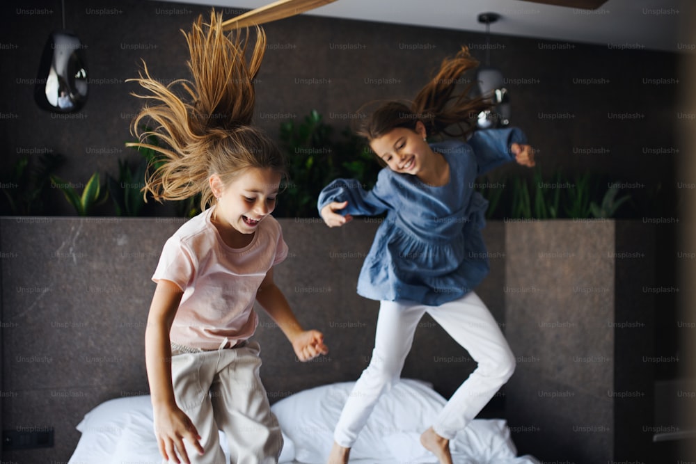 Two little sister jumping on a bed indoors in hotel.
