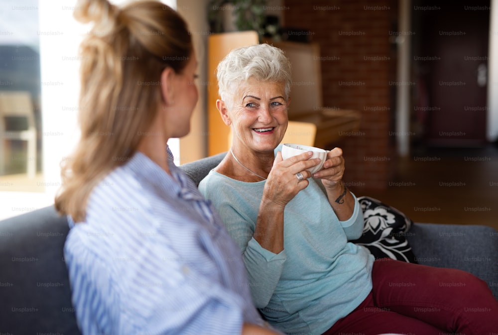 A happy senior mother having coffee with adult daughter indoors at home, sitting and talking.