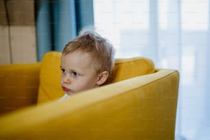 Una niña curiosa sentada en el sofá y mirando hacia otro lado.