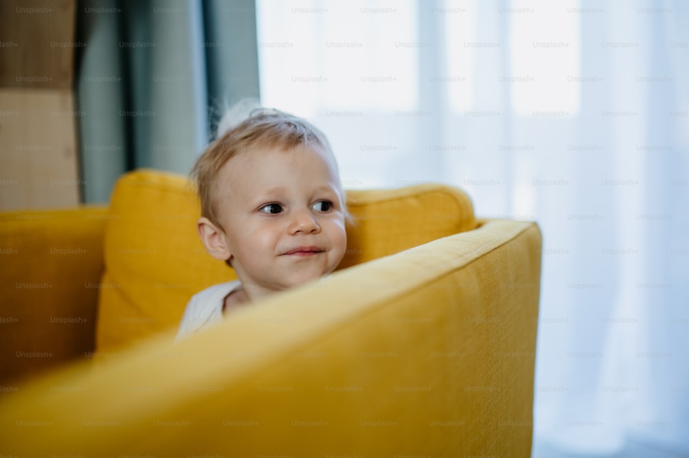 Un petit garçon curieux assis sur un canapé et détournant le regard.