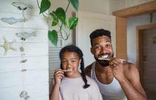 A happy young father with small daughter brushing teeth indoors at home, sustainable lifestyle.