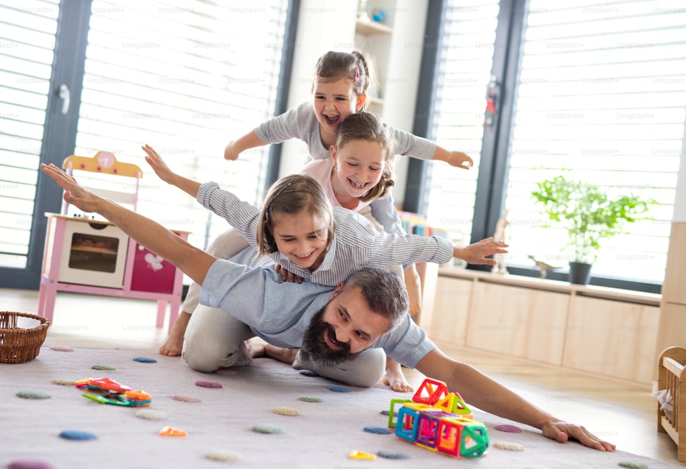 Un padre con tres hijas en casa adentro, jugando en el suelo.