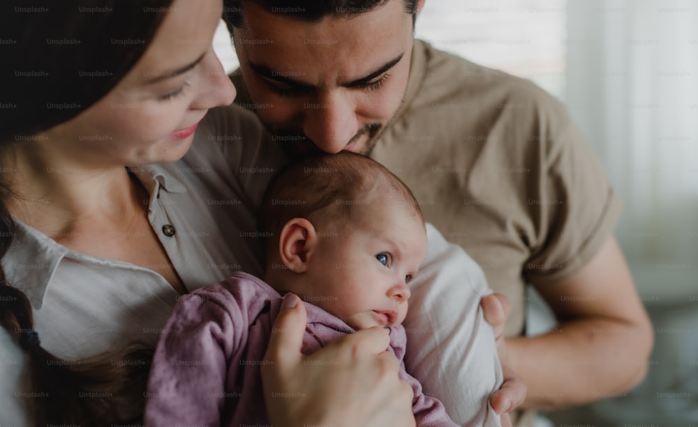 Close up of happy young parents holding and kissing their newborn baby indoors at home