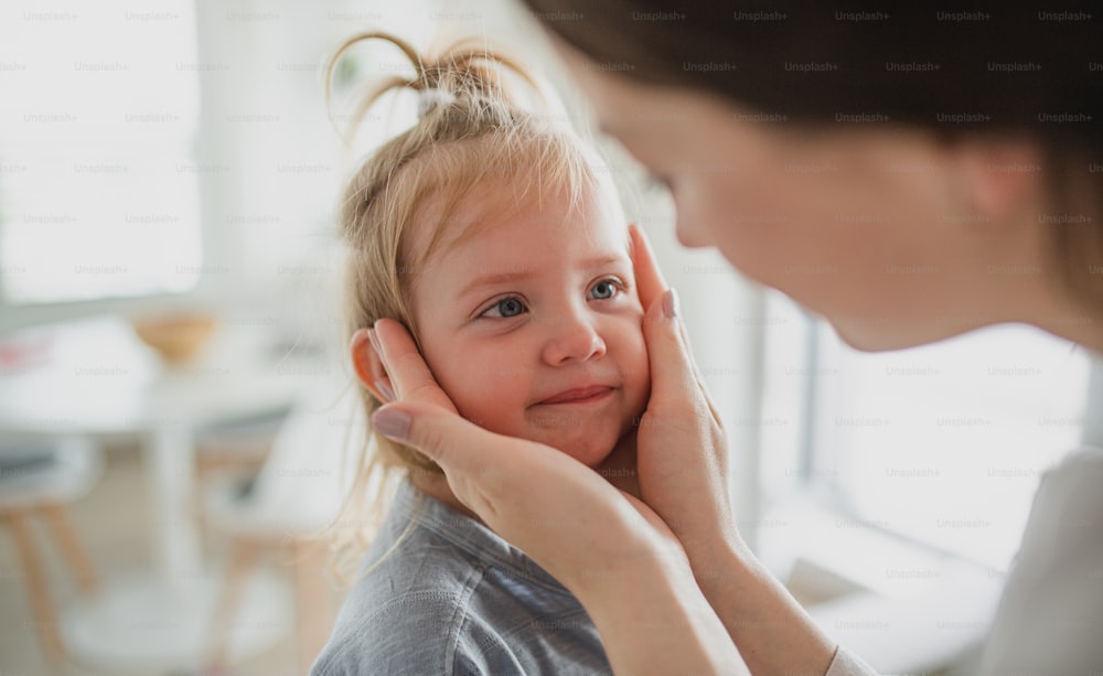 An unrecognizable young mother holding her little daughter face, indoors at home.