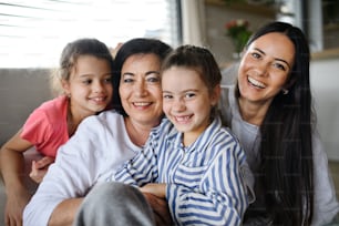 Happy small girls with a mother and grandmother indoors at home, sitting on floor and looking at camera