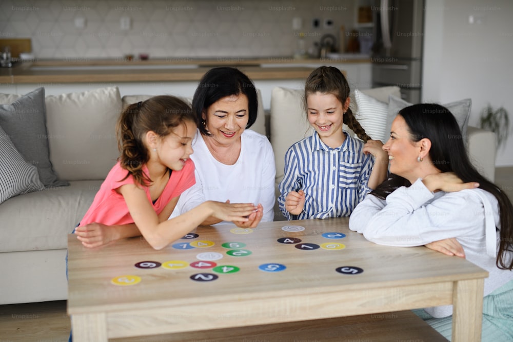 Happy small girls with a mother and grandmother playing cards indoors at home.