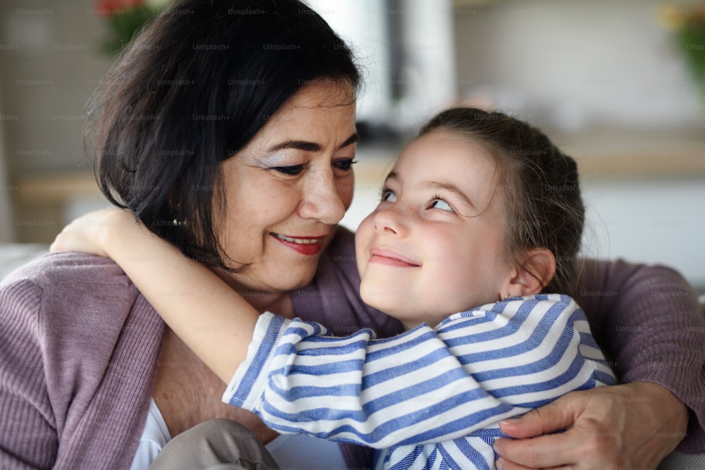 A close up of happy small girl with senior grandmother indoors at home hugging.