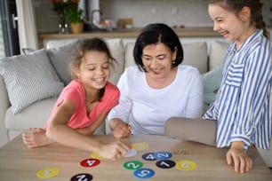 Piccole bambine felici con una nonna che gioca a carte in casa a casa.