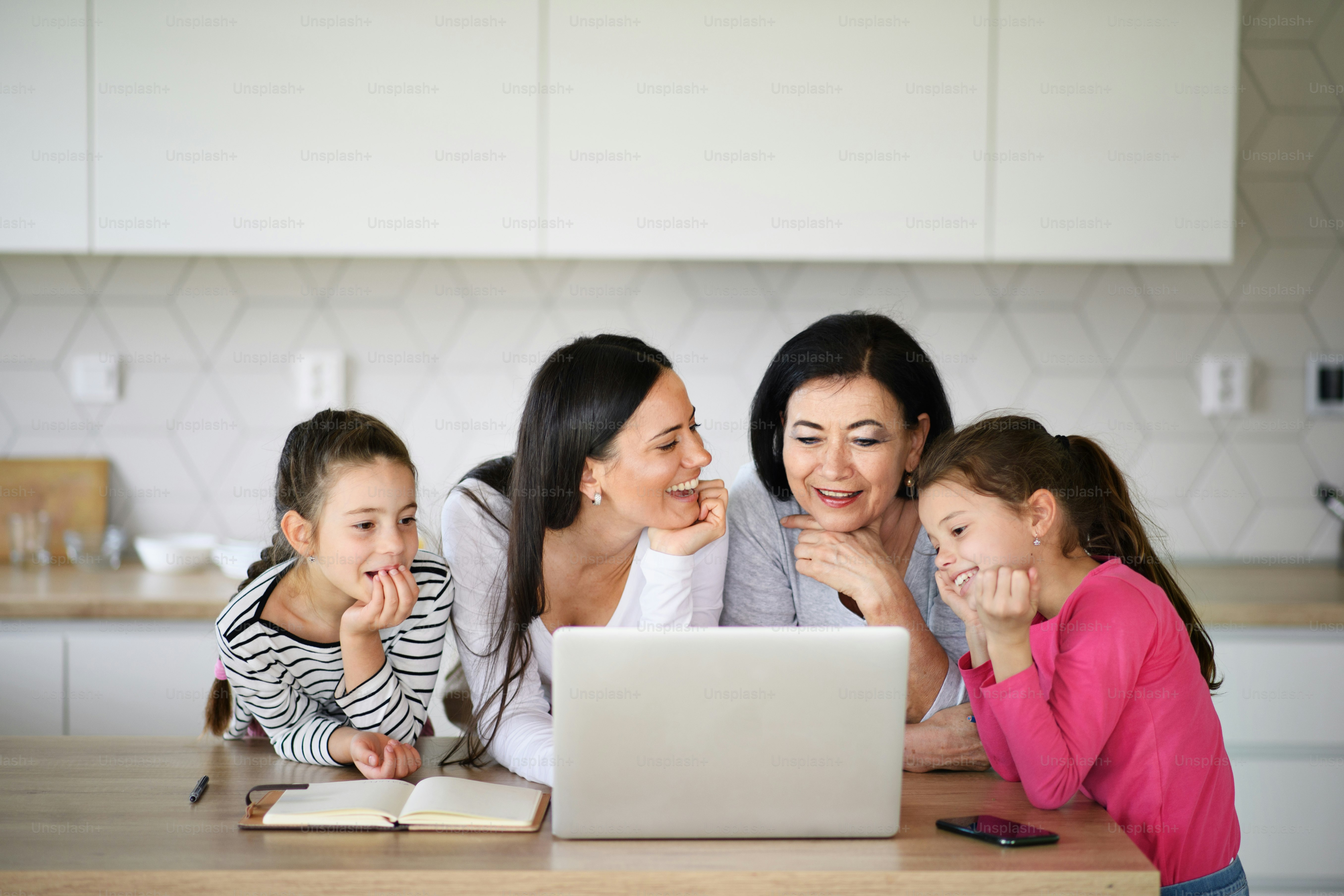 Gadis-gadis kecil yang bahagia dengan ibu dan nenek di dalam ruangan di rumah, menggunakan laptop.