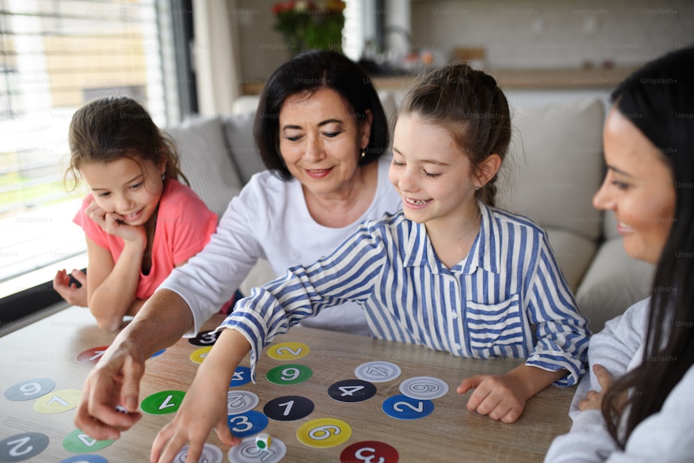 집에서 실내에서 카드 놀이를 하는 어머니와 할머니가 있는 행복한 어린 소녀들.
