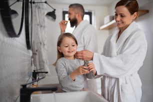 A father and mother with small daughter washing indoors in bathroom in the evening or morning.