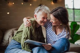 A portrait of happy senior mother with adult daughter indoors at home, using tablet.