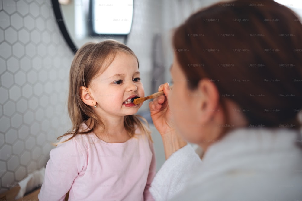 Mother with happy small daughter brushing teeth indoors in bathroom in the evening or morning.