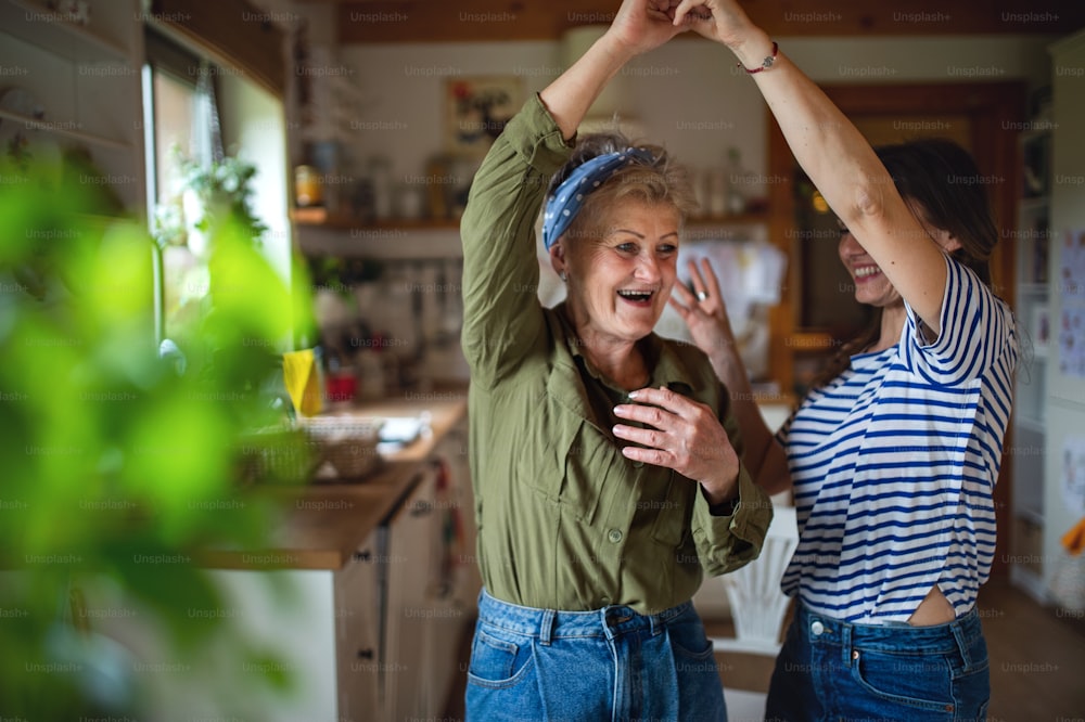 A cheerful senior dancing with adult daughter indoors at home, having fun.