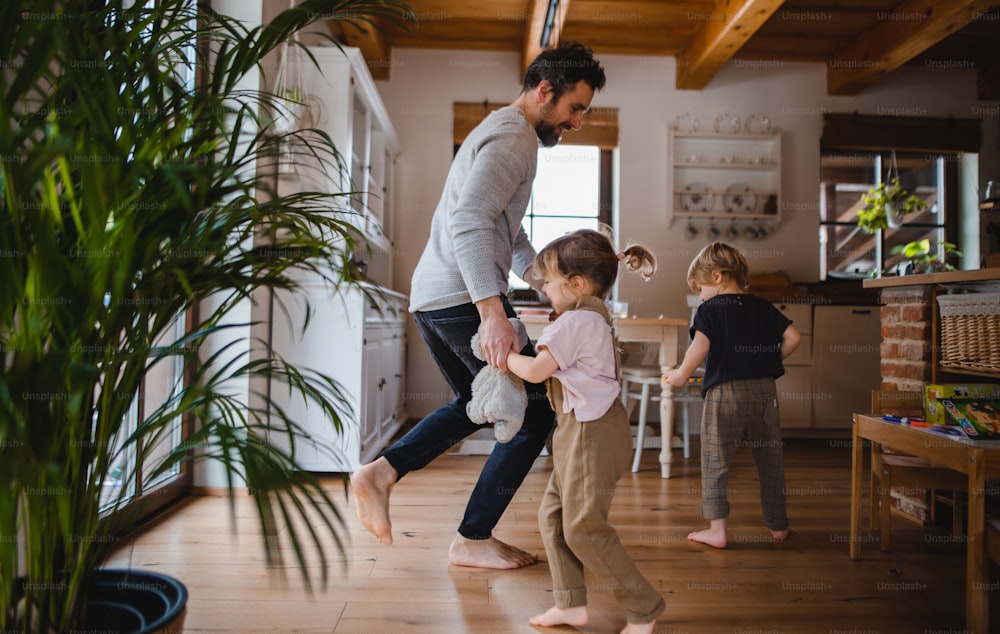 A mature father with two small children dancing indoors at home.