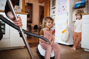 An unrecognizable father with small children hoovering indoors at home, daily chores concept.