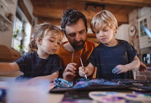 A mature father with two small children resting indoors at home, painting pictures.