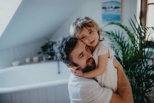 Mature father with a small daughter indoors in bathroom at home.